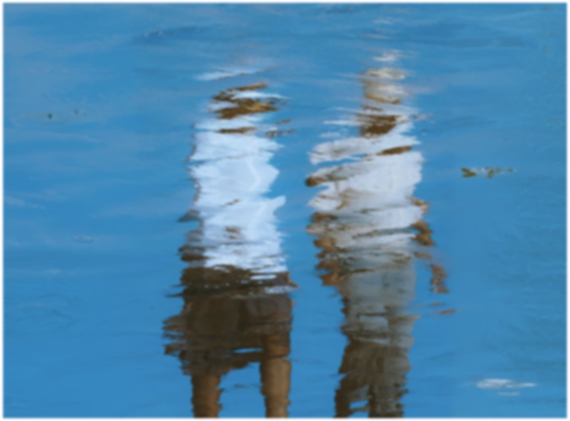 Reflections of two people rippling across blue water